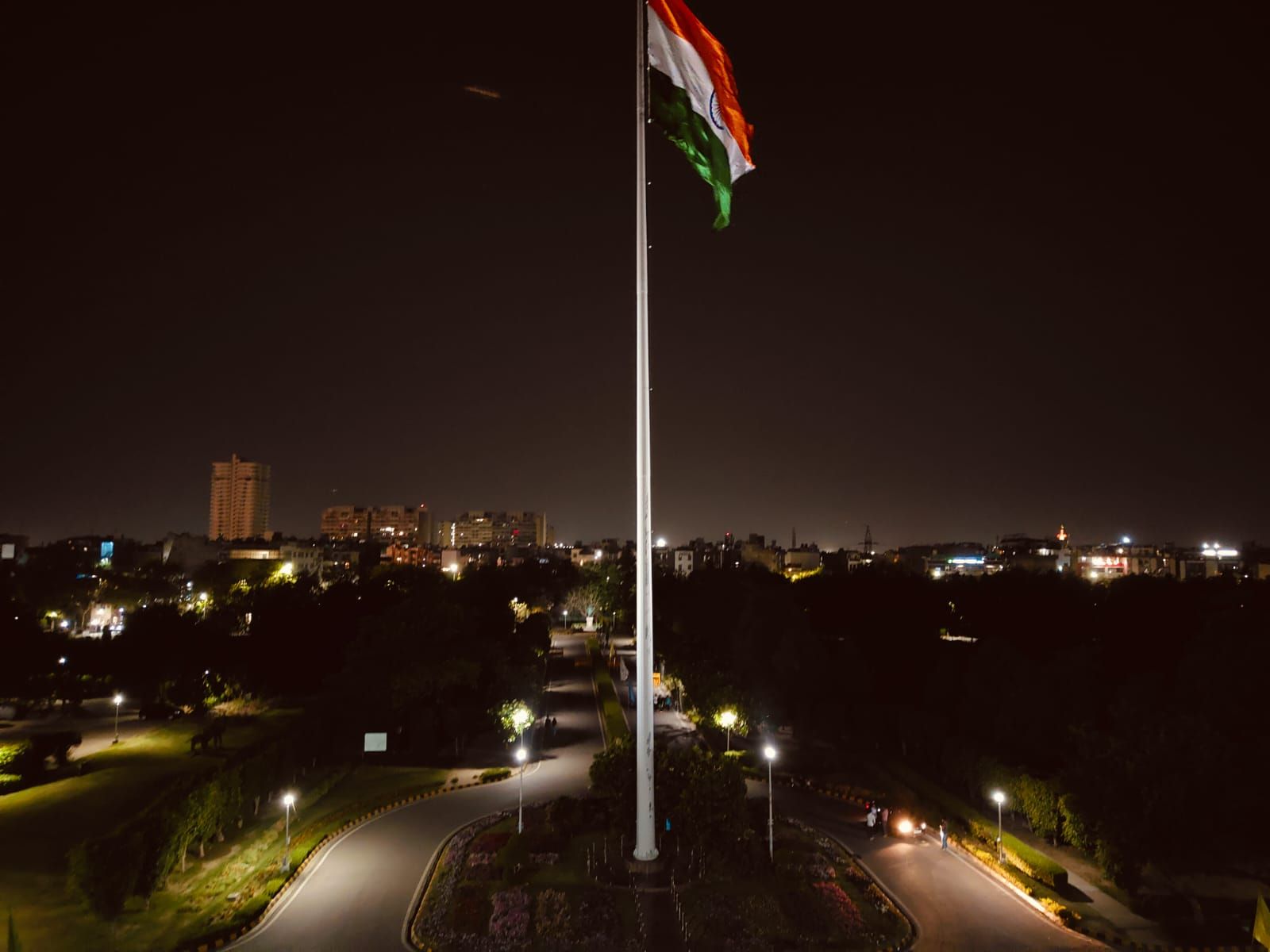 An Indian flag above a lit flagpole overlooking a city park at night