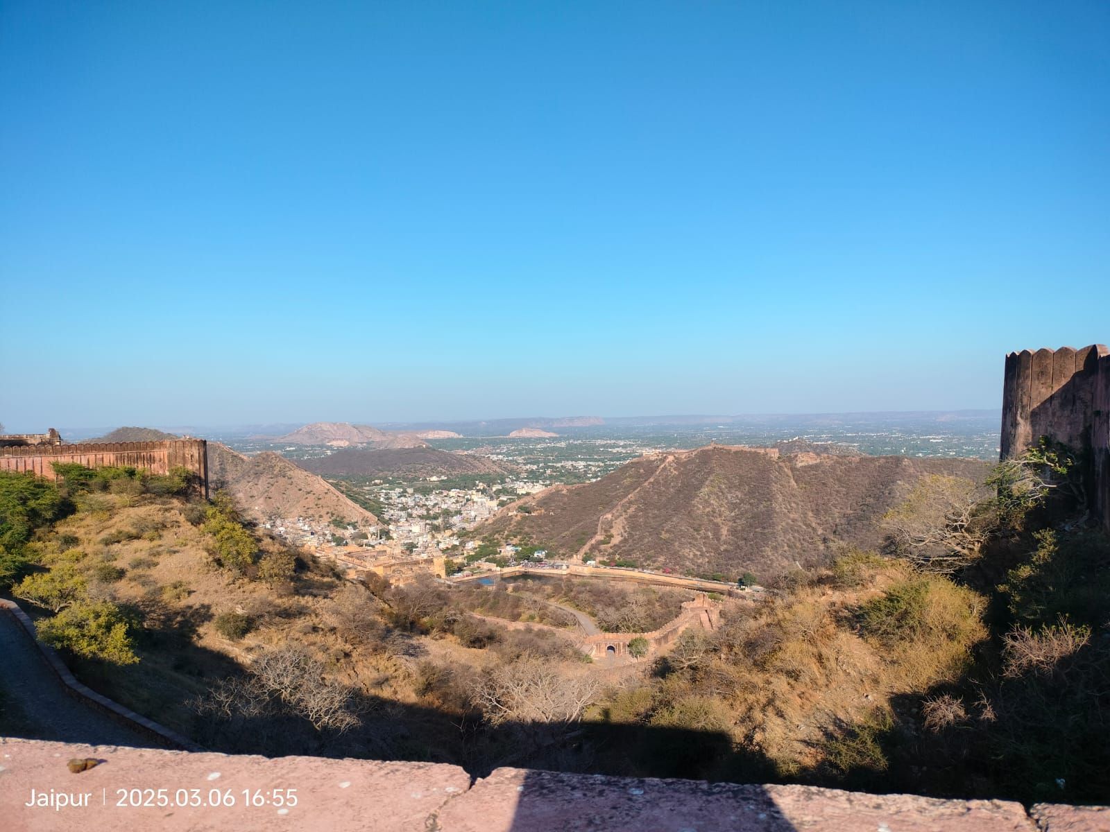 A wide view across sunlit hills, fort walls, and a city in the valley